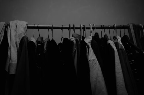 Wieszak z ciasno upchanymi ubraniami w ciemnym świetle – symbol przepełnionej szafy, z której trzeba coś wyrzucić, by zrobić miejsce na nowe podejście.