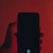 Telefon w dłoni, rozświetlony czerwienią – symbol uzależnienia i kontroli