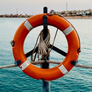 Pomarańczowe koło ratunkowe zawieszone nad wodą, symbolizujące plan awaryjny i utrzymanie się na powierzchni w trudnych momentach.