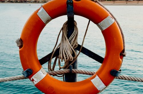 Pomarańczowe koło ratunkowe zawieszone nad wodą, symbolizujące plan awaryjny i utrzymanie się na powierzchni w trudnych momentach.