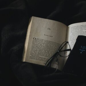 Detoks dopaminowy – książka i okulary obok telefonu symbolizują wybór między skupieniem a rozpraszaczami.